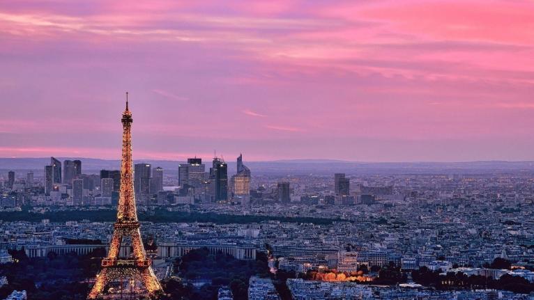 drone view of paris from behind the eiffel tower with sky glowing pink at sunset